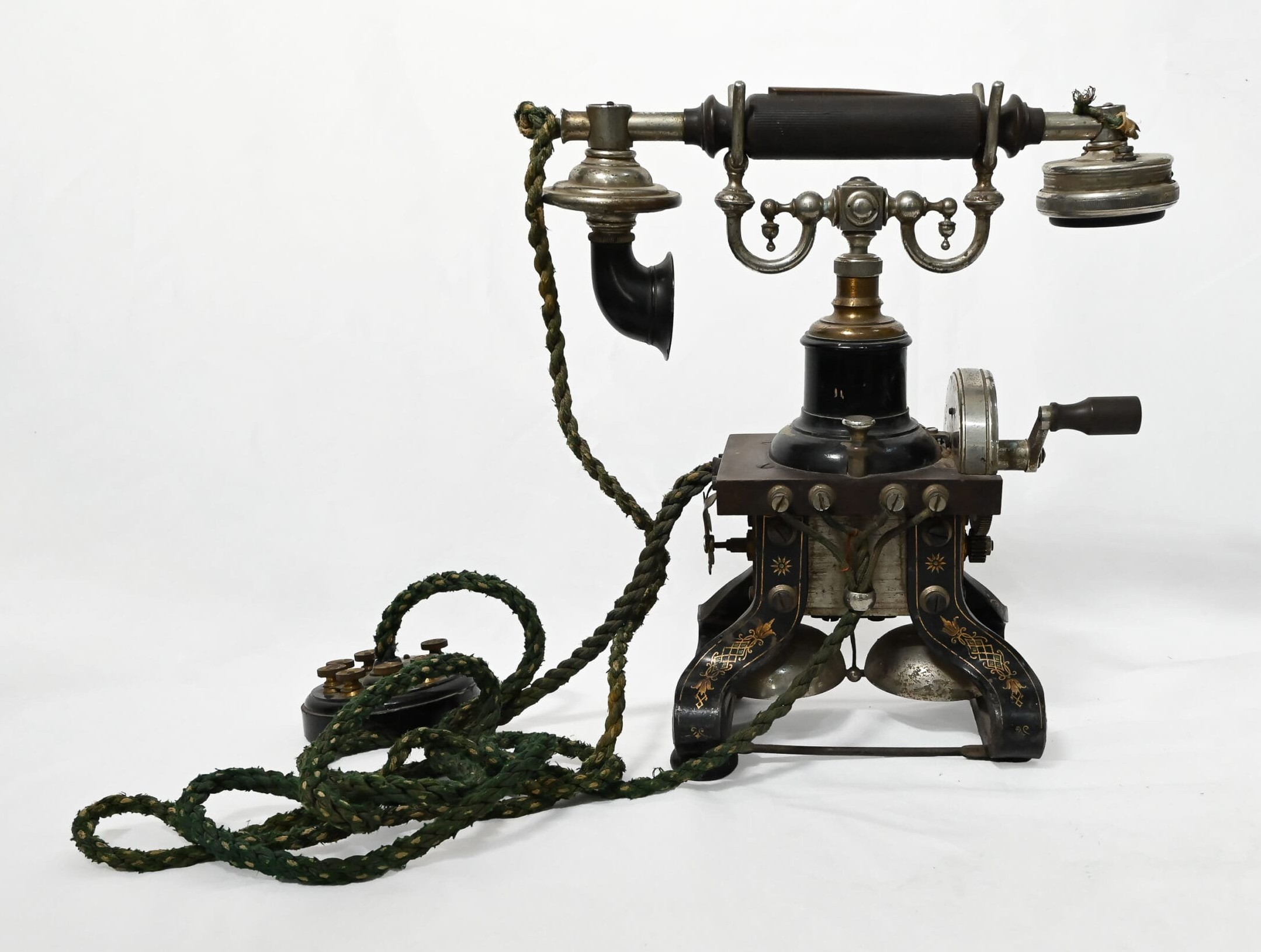 Metal 'skeleton' telephone sitting on a small wooden and metal stand with a crank handle.